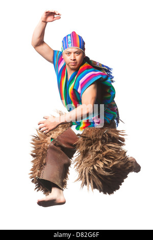 A man is captured mid-motion in a dynamic dance pose, wearing vibrant traditional clothing. He is barefoot and dressed in a multicolored striped vest and matching hat, both featuring bright rainbow Stock Photo