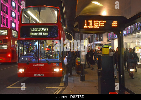 Bus stop shelter night timetable indicator board people boarding red Metroline double decker bus & driver Oxford Street West End London England UK Stock Photo