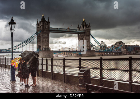 LONDON, UK - JULY 17, 2011:  Family sheltering from heavy rain under umbrellas by Tower Bridge, London Stock Photo