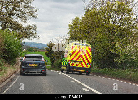 View through a windscreen of an ambulance with blue lights flashing rushing to an emergency overtaking a car along A5 road. UK Stock Photo