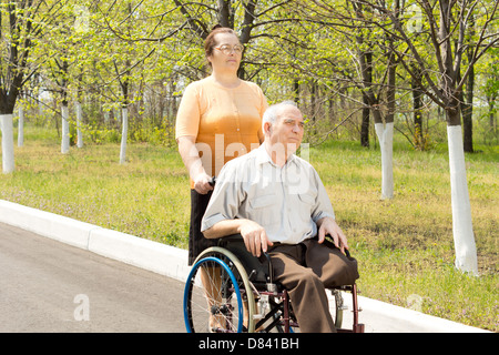 Elderly amputee with one leg amputated above the knee being taken for a walk in a wheelchair by his wife or carer Stock Photo