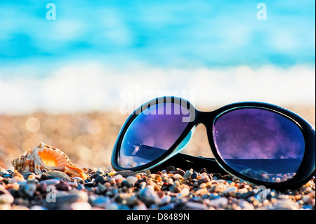 Sunglasses and shells lie on the shingle beach sea Stock Photo