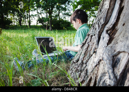 boy using his laptop outdoor in park on grass Stock Photo