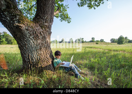 boy using his laptop outdoor in park on grass Stock Photo