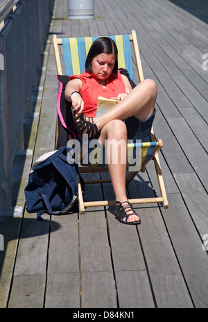 Enjoying the sunshine - woman sat in deckchair reading a book on Bournemouth pier in May Stock Photo