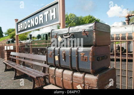 Old vintage trunks with labels stuck on them piled up on a platform by a bench and a large Bridgnorth sign at Severn Valley