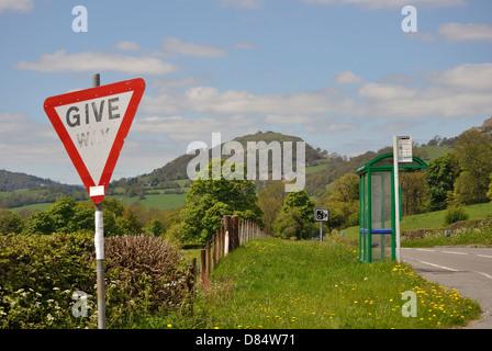 A faded give way sign in front of a bus stop, with a speed camera sign in the distance. Stock Photo