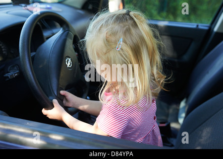 Young child blond girl sitting in driver seat of car Stock Photo