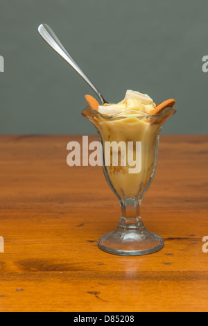 A dessert glass full of banana pudding, with spoon. Sitting on a wooden table, closeup. Oklahoma, USA..