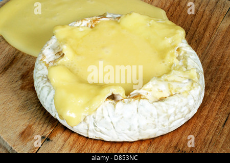 Baked whole French Camembert with cheese oozing out onto a wooden cheese board. Stock Photo