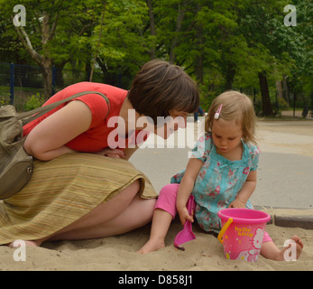 2 year old little girl with mother in sand pit playing toys playground Stock Photo
