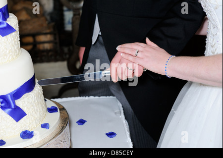 Closeup of bride and grooms hands cutting cake and showing rings Stock Photo