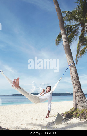 man lying in hammock talking on mobile phone. Stock Photo