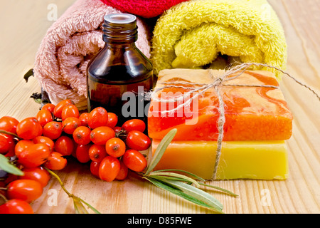 Oil in a bottle, two homemade soap, towels, twig and berries of sea buckthorn on a wooden board Stock Photo