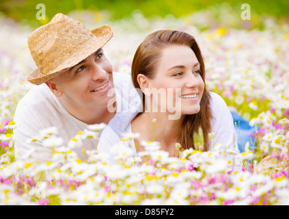 Closeup portrait of beautiful couple lying down on chamomile meadow and looking in one side, summer weekend, happiness and love Stock Photo