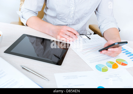 Young successful businesswoman sitting at desk in the office and using mobile phone for business communication Stock Photo
