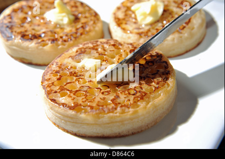 Spreading butter with a knife on a hot toasted crumpet for breakfast or tea Stock Photo