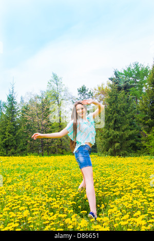 Beautiful joyful happy attractive carefree young girl (woman) dancing and jumping in summer (spring) park on yellow dandelions. Stock Photo