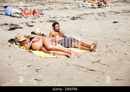 An expecting pregnant couple laying out on the beach Stock Photo