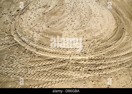 Tractor Tyre tracks in a loop and footprints on sand Stock Photo