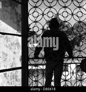 Man on the balcony of an abandoned house, metal door pattern. Black and white. Stock Photo