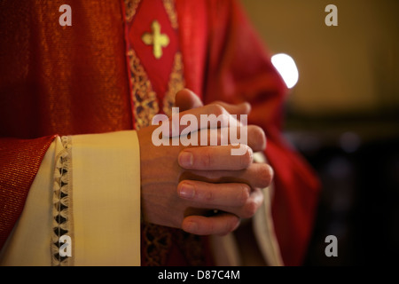 Catholic priest on altar praying with hands joined during mass service in church Stock Photo