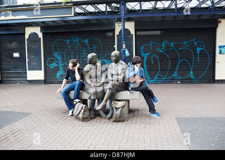 Two young men act as bookends to a sculpture of two women sitting talking on a bench in Dublin city centre Stock Photo