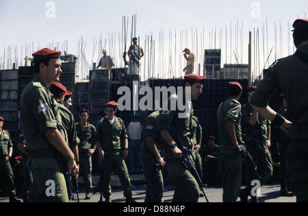 Israeli soldiers from the 35th Brigade, also known as the Paratroopers Brigade walk past Palestinian workers in a construction site in Jerusalem Israel Stock Photo