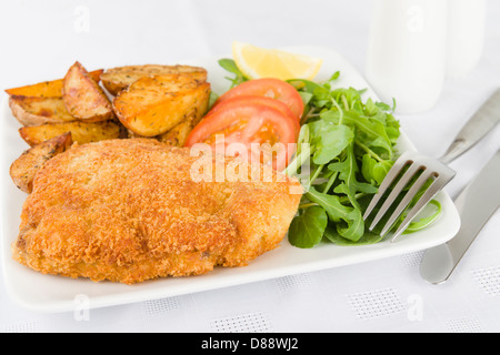 Wiener Schnitzel - Veal steak breaded and fried in butter served with salad, potato wedges and a lemon slice. Stock Photo