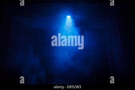 Smoke creates a misty haze in front of a blue light, on a dark stage. Stock Photo