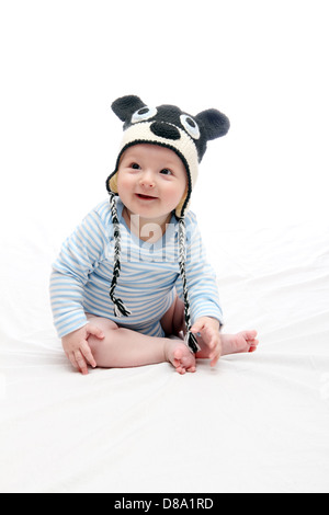beautiful laughing happy baby boy sitting on white bed in knitted hat Stock Photo