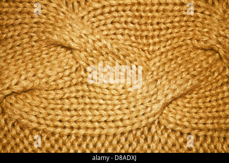 A close-up of a gold-colored cable knit fabric pattern, showcasing the detailed weaving and texture of the textile. This design is often used in knitwear. Stock Photo
