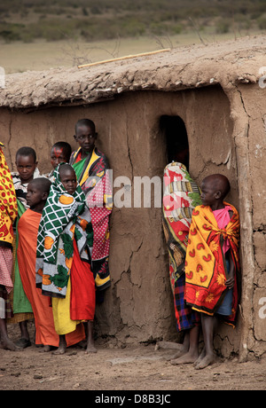 Masai Children, wearing traditional clothing, standing in front of a mud hut in a village in the Masai Mara, Kenya, Africa