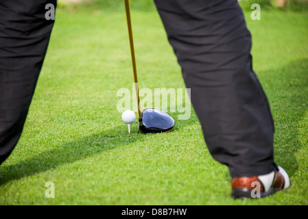 a golfer addresses the golf ball with a driver in the tee box