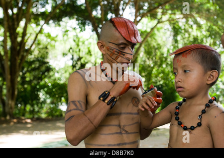 Young native of the ethnic group Tsachila paints the body of a child in the community Stock Photo