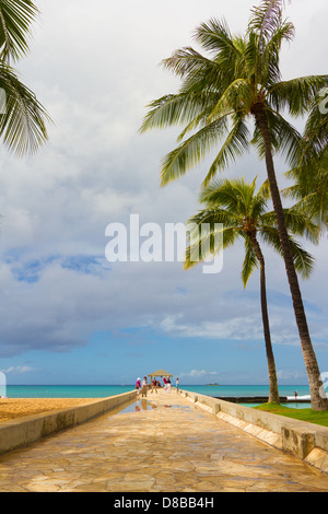 Stone walkway out to Pacific Ocean with palm trees overhead at Waikiki Beach in Hawaii Stock Photo
