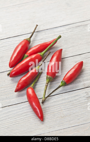 Seven red Thai chillies on a rustic wood surface. Stock Photo