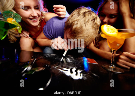 Image of young guy sniffing cocaine surrounded by two girls in night club Stock Photo