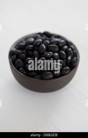 A small bowl of black beans on a white wood surface. Stock Photo
