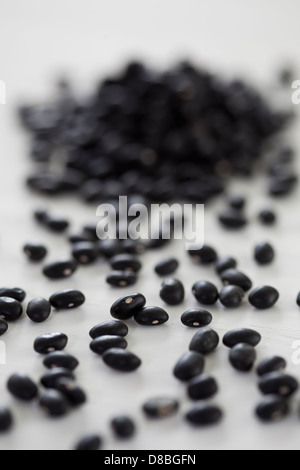 A scattering of black beans on a white wood surface. Stock Photo