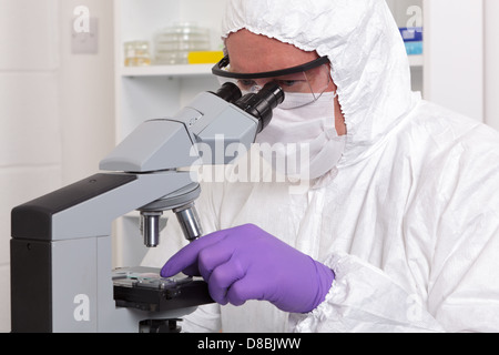 A lab technician in sterile clothing adjusting a slide whilst examining the sample through a microscope. Stock Photo
