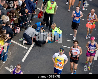 Race officials and St John Ambulance help a collapsed male competitor in 2013 London marathon Victoria Embankment England Europe Stock Photo