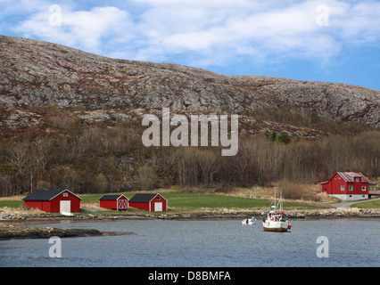 Traditional small Norwegian village with red wooden houses on rocky coast and small fishing boat nearby Stock Photo