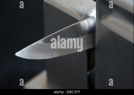 The point and tip of a slicing style kitchen knife, with its edge in a sharpening tool. Stock Photo