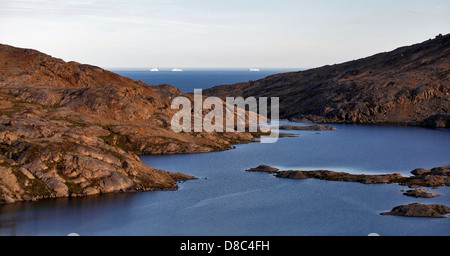 Small bay with icebergs floating at the open ocean in the background, near Kulusuk, Greenland Stock Photo