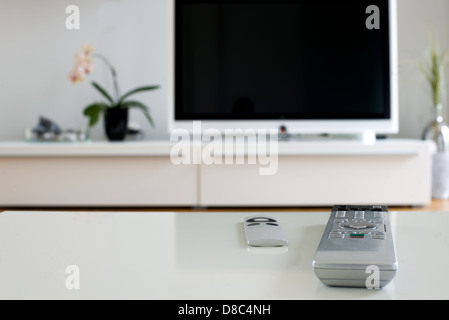 two remotes on white table in front of television Stock Photo