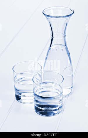 Water Carafe and Two Glasses - a carafe of water on a table with two glasses, blue toned. Stock Photo