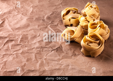 Fettucine Pasta on Brown Paper Background - fettucine or tagliatelle or pappardelle pasta on a background of crumpled... Stock Photo