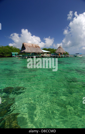 Clear waters, thatched roof bungalows and tourists at jetty in Coral Cay restaurant Stock Photo