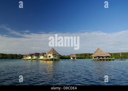 Thatch roofed bungalows on stilts in lagoon at Punta Caracol Aqua Lodge Stock Photo